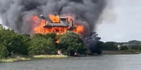 A view of a home on fire near a body of water.