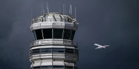 An airplane flies near a control tower on a dark cloudy day