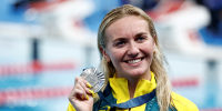 Ariarne Titmus smiles while holding onto a silver medal that she's wearing around her neck