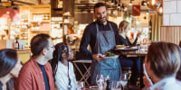 Waiter serving food to customers during party in restaurant.