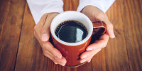 Hands holding a mug of black coffee