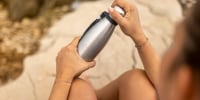An unrecognizable woman closes a stainless steel water bottle.