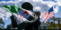 A man holds a Syrian flag across the street from the White House.