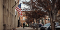 A view of the exterior of a building with an American flag on the side, facing a sidewalk and parking lot