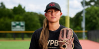 Kelsie Whitmore stands outside on the baseball field holding a baseball glove