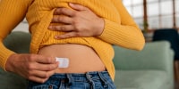 Unrecognizable woman in the comfort of her home applies a hormone replacement therapy patch to her waist.
