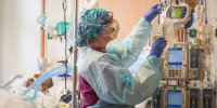 A nurse grabs a vial inside of a room with a patient inside