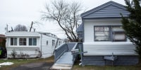 A '"for sale" sign is seen in a window of a mobile home