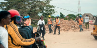 People walk and ride motorbikes along a dirt road