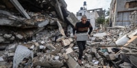 A person holds a cinderblock while walking on top of rubble outside
