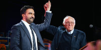 Zohran Mamdani, left, and Bernie Sanders stand together on stage and hold hands while raising them up