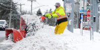 A man uses a snow blower to clear snow outside