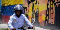 A motorcycle rider passes in front of an oil-themed mural.