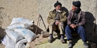 Afghan men sit next to sacks of flour outside