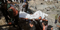 People carry a body wrapped in white tarp out from the rubble