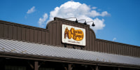 The orange and white Cracker Barrel logo is displayed on a brown building's facade, under clear blue skies.