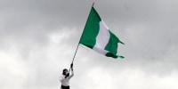 A person on the roof of a building waves a Nigerian flag