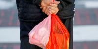 A pedestrian carries plastic shopping bags.