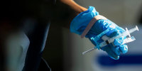 A blue gloved hand holds a syringe
