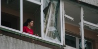A resident of a building damaged by a drone attack looks out of a shattered window in Kharkiv, Ukraine