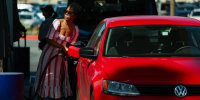 A woman pumps gasoline into her vehicle at a gas station.