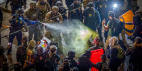 Law enforcement spray tear gas at protesters.