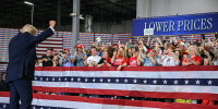 Attendees at a Trump rally cheer as he pumps his fist toward them with his back to the camera