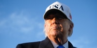 Donald Trump wears a white baseball cap with the acronym USA on the front