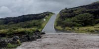 A view of flood waters in the front of a hilly road and grassy planes