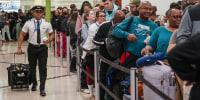 A pilot walks past travelers waiting in line at a Transportation Security Administration (TSA) checkpoint at Hartsfield-Jackson Atlanta International Airport (ATL) in Atlanta, Georgia, US, on Friday, March 20, 2026.