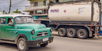 Image: An old American car drives past a truck belonging to a private Cuban company (mipyme) parked in front of a gas station with an IsoTank of imported fuel in Havana
