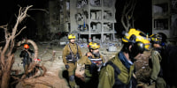Israeli security forces and rescue teams work at the site struck by an Iranian missile, illuminated by flash at night