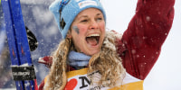 Jessie Diggins smiles while holding two skis in a snowstorm.
