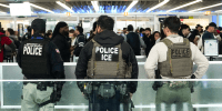 Three ICE agents watch a line of people inside of an airport
