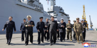 Kim Jong Un walking on a cement platform surrounded by other men in uniform.