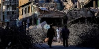 Sudanese men walk past destroyed building in the capital Khartoum.