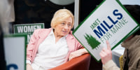 Janet Mills sits and speaks to someone holding a sign over their face that reads "Janet Mills for Maine"