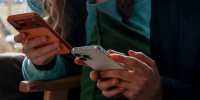 two teenagers aged 14-years-old look at their iPhone screens.