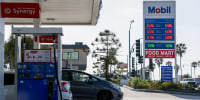 Image: Vehicles sit parked at fuel pumps as regular gasoline prices above $6 per gallon and diesel prices above $7 per gallon are displayed outside a Mobil gas station 