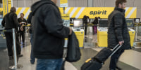 People walk by Spirit Airlines counters inside an airport.