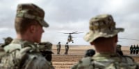 Soldiers look at a plan taking off in the distance outside