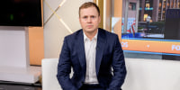 Spencer Pratt seated on a white couch with his hands folded in his lap.