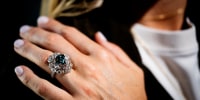 A large blue-green diamond rin on a person's hand seen in a close-up view.