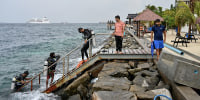 Three men wearing diving equipment make their way up a staircase from the water. 