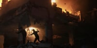 A person silhouetted by the flames of a burning building at night.