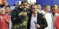 Nicolas Maduro and Alex Saab stand together with microphones in a crowd.