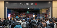 Dozens of young adults dressed in dark jackets congregate outside a Swatch retail store in a shopping mall.