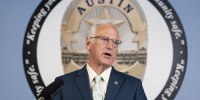 Kirk Watson speaks during a press conference in front of the seal of the AUstin Police Department.