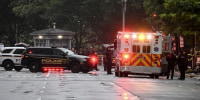 An ambulance and other law enforcement vehicles parked with their lights flashing on a wet city street.