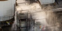An aerial photo of three large industrial tanks with water being sprayed and misted onto them.